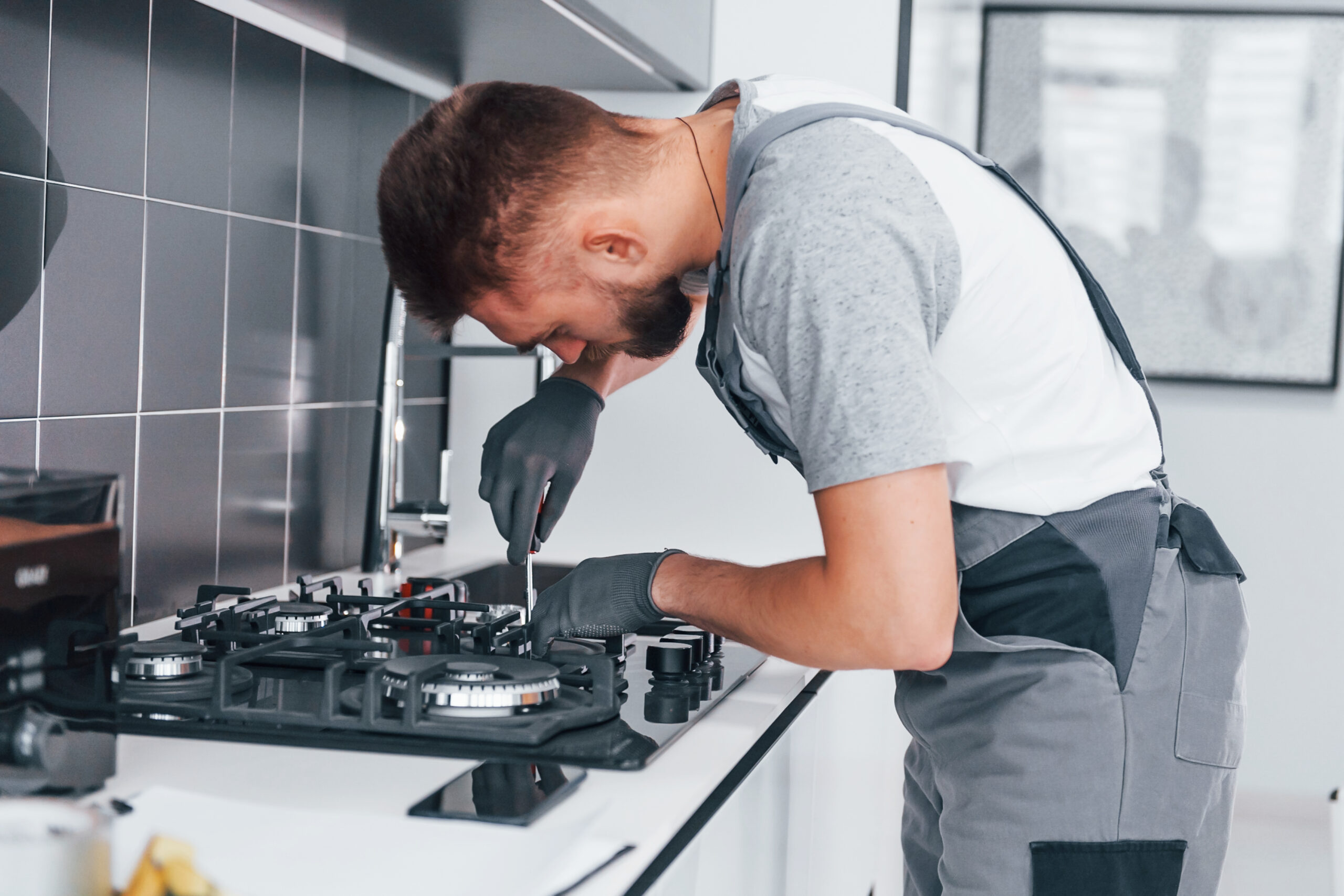 Young professional plumber in grey uniform working on the kitchen